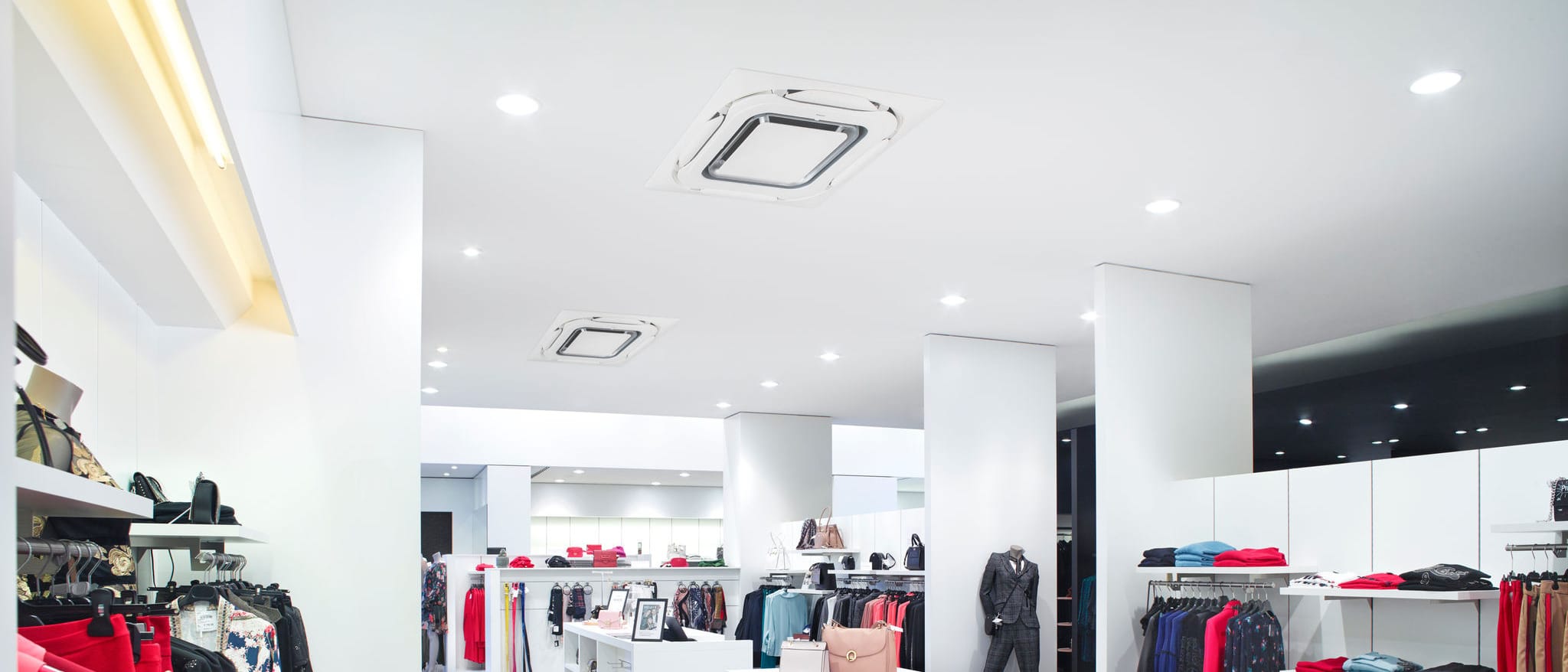 Dvi „Daikin Round Flow“ FCAG50B kasetės su baltu dizaino skydeliu šviesios drabužių parduotuvės lubose
