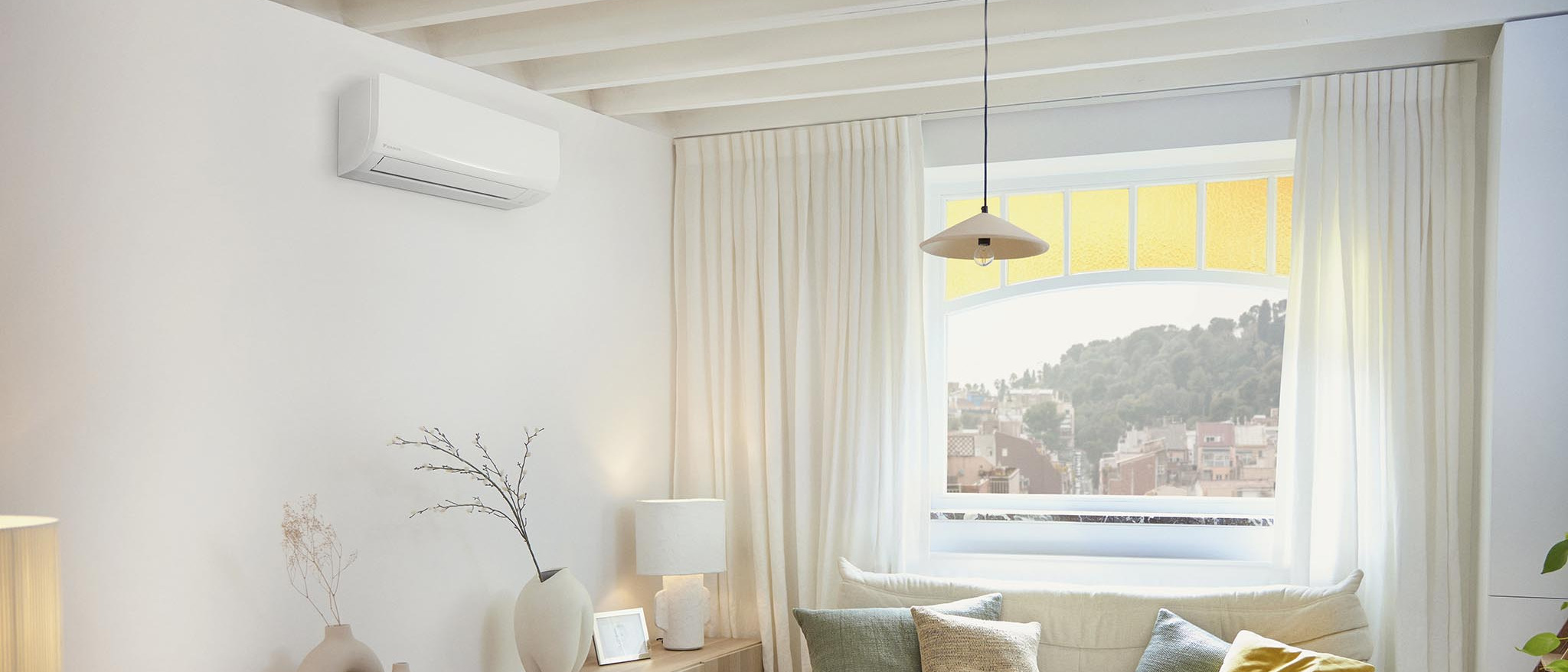 Baltas Daikin Sensira FTXF42F vidinis blokas šviesioje svetainėje su dideliu langu