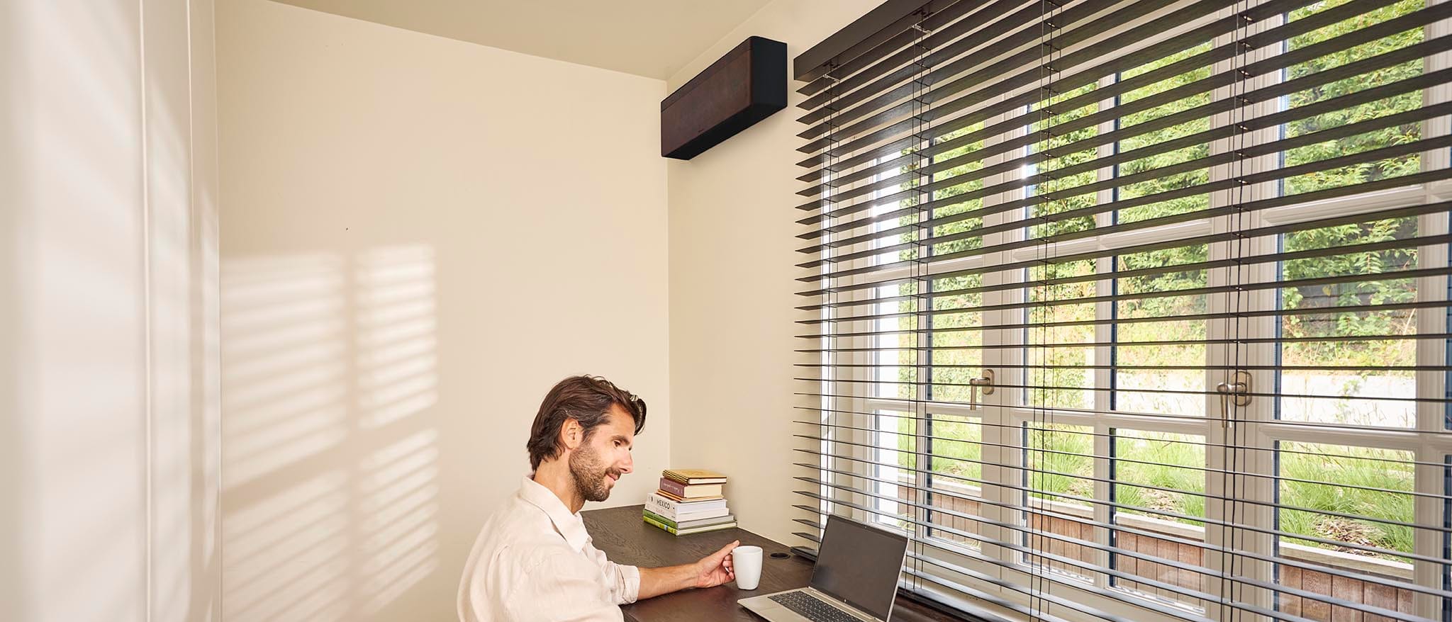 Daikin Stylish FTXA25DL su tamsiai rudos odos stiliaus skydeliu ir juodu korpusu šviesiame darbo kambaryje