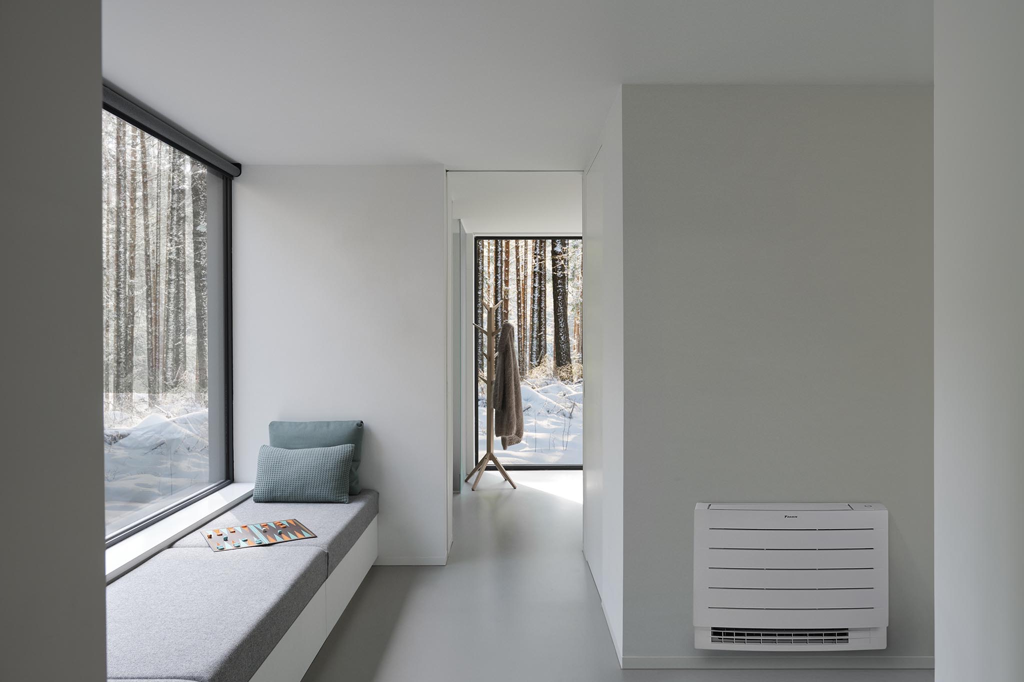 Kompaktiškas Daikin Perfera grindinis blokas, pakabintas ant sienos šalia lango