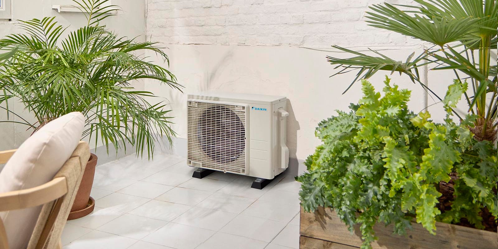 Daikin Sensira RXF42F RXF-F lauko blokas šviesiame kiemelyje tarp augalų